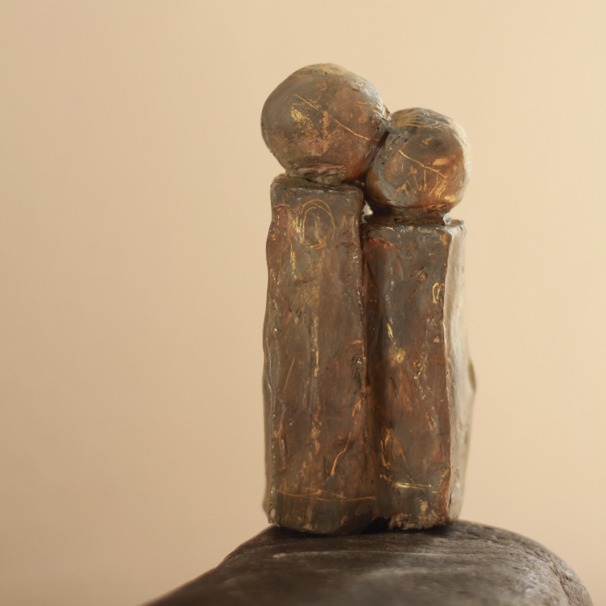 Two golden-brown clay columns with round heads leaning towards each other, with fine gold lines etched into the surface