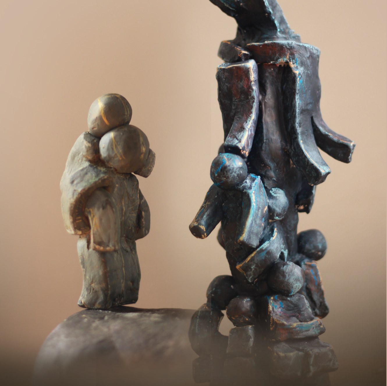 Two small dark clay sculptures of figures against a warm beige background