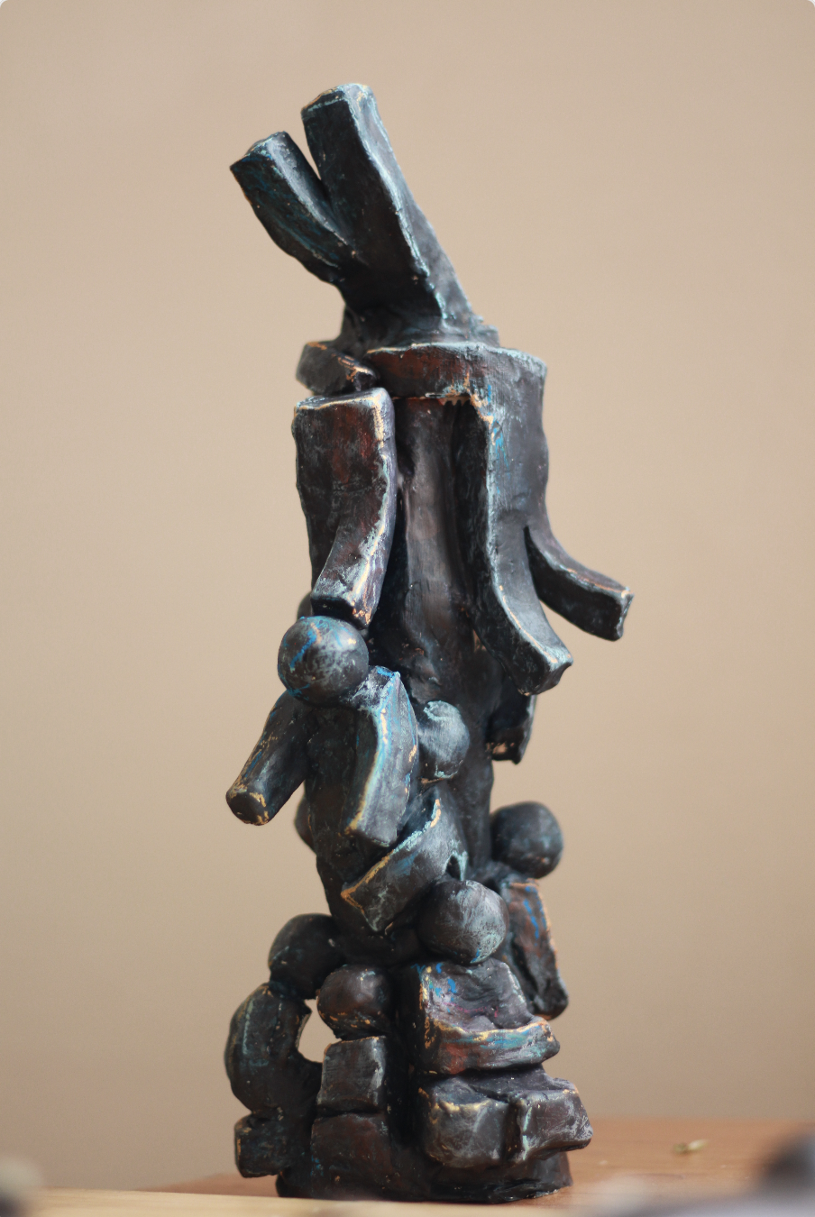 Tall dark clay sculpture made of angular slabs and round shapes with blue and gold highlights