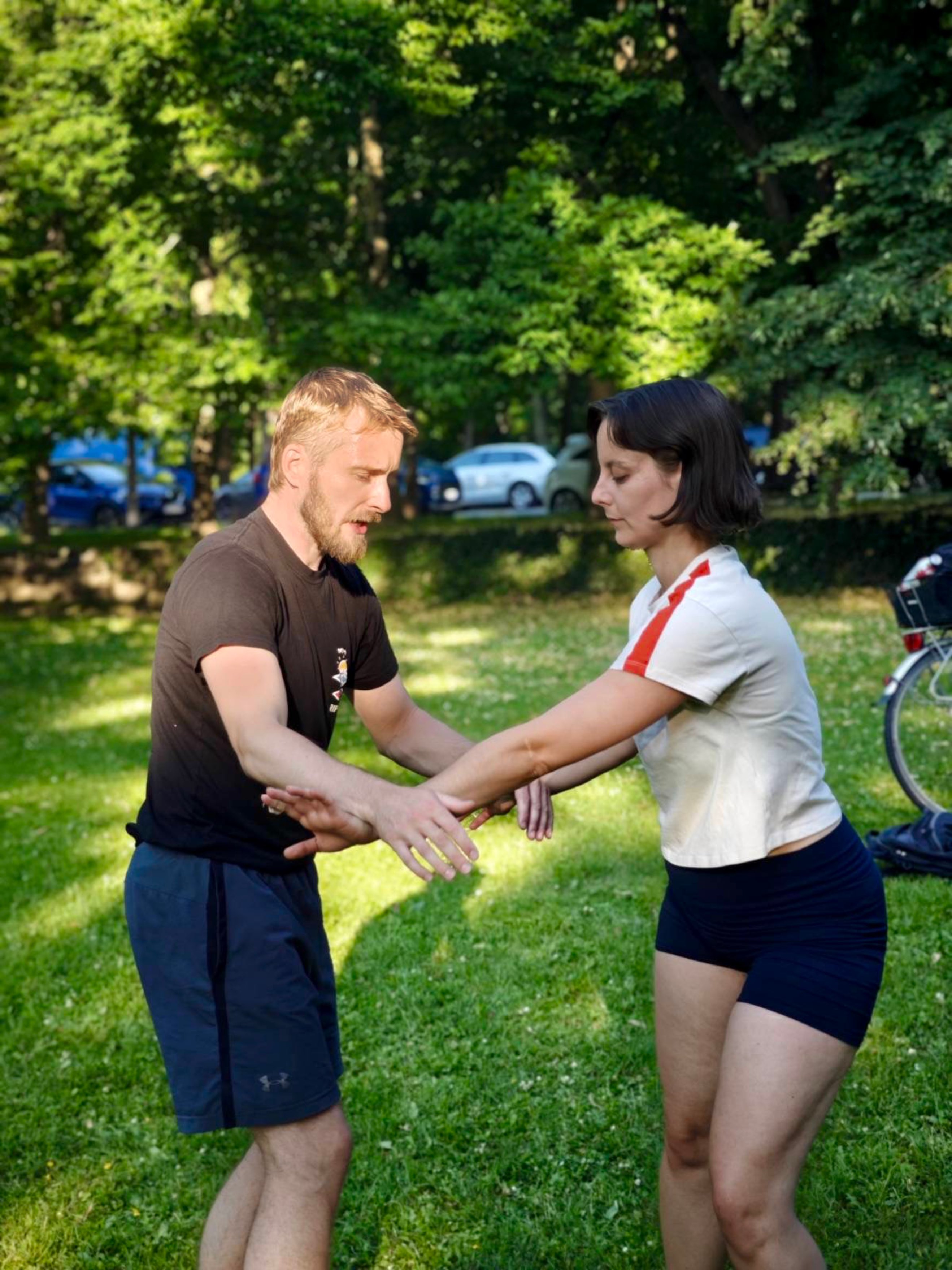 Sam guiding a partner through a slow arm exercise in a park
